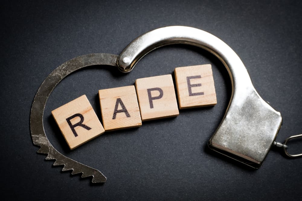 The word made of wooden letters - rape, on a black background in a handcuff. 