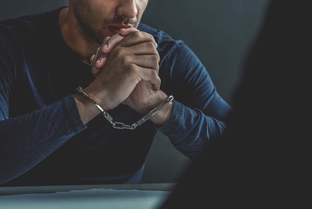 Criminal man with handcuffs in interrogation room being interviewed after probation violation