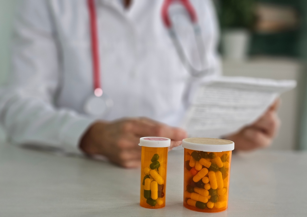 Two prescription bottles of pills on a table in front of a doctor reading a document